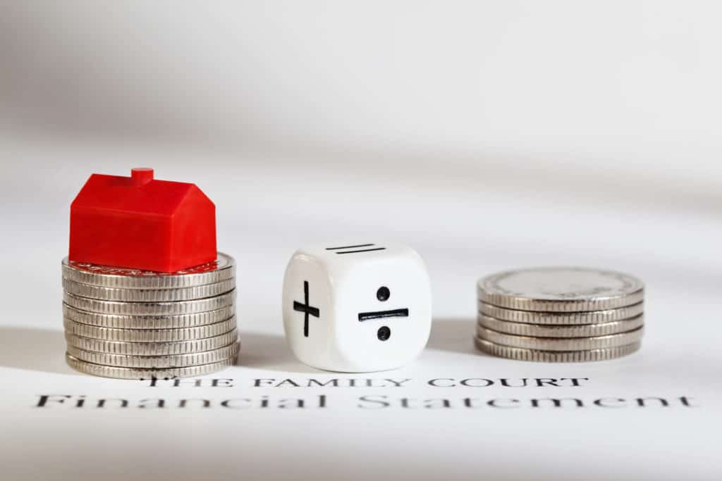Divorce financial settlement: a toy house on coins beside a dice marked plus and divide, on a Family Court financial statement
