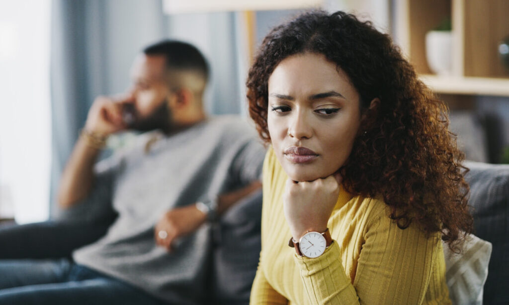 Toxic relationship or abuse: a couple sitting apart on a sofa while one partner looks away, lost in thought