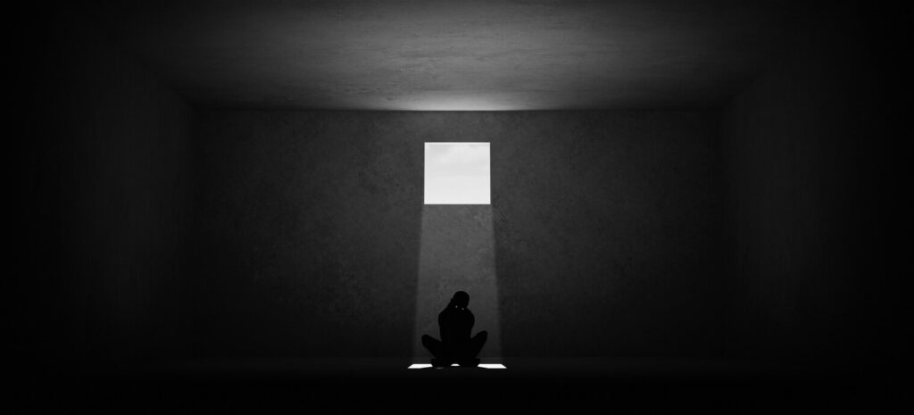 Reactive abuse and its aftermath: a lone figure sits hunched on a concrete floor beneath a single square of daylight