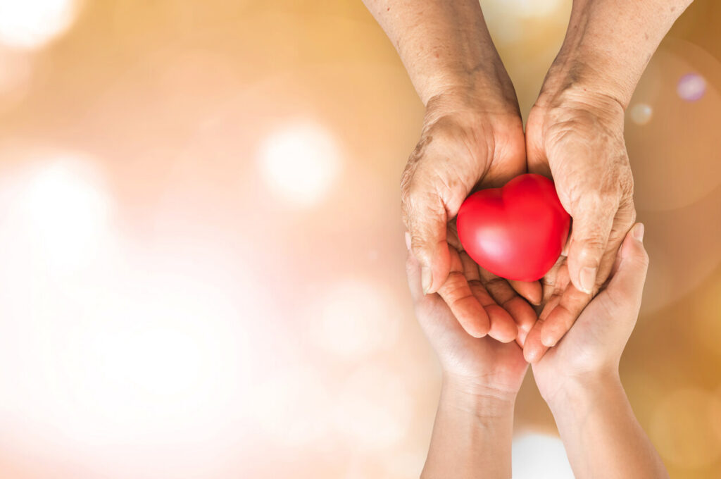 Adopt an adult: older hands passing a red heart into a younger adult's open hands