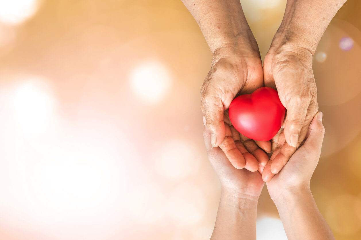 Adoption contact register: older hands passing a red heart into a younger adult's open hands