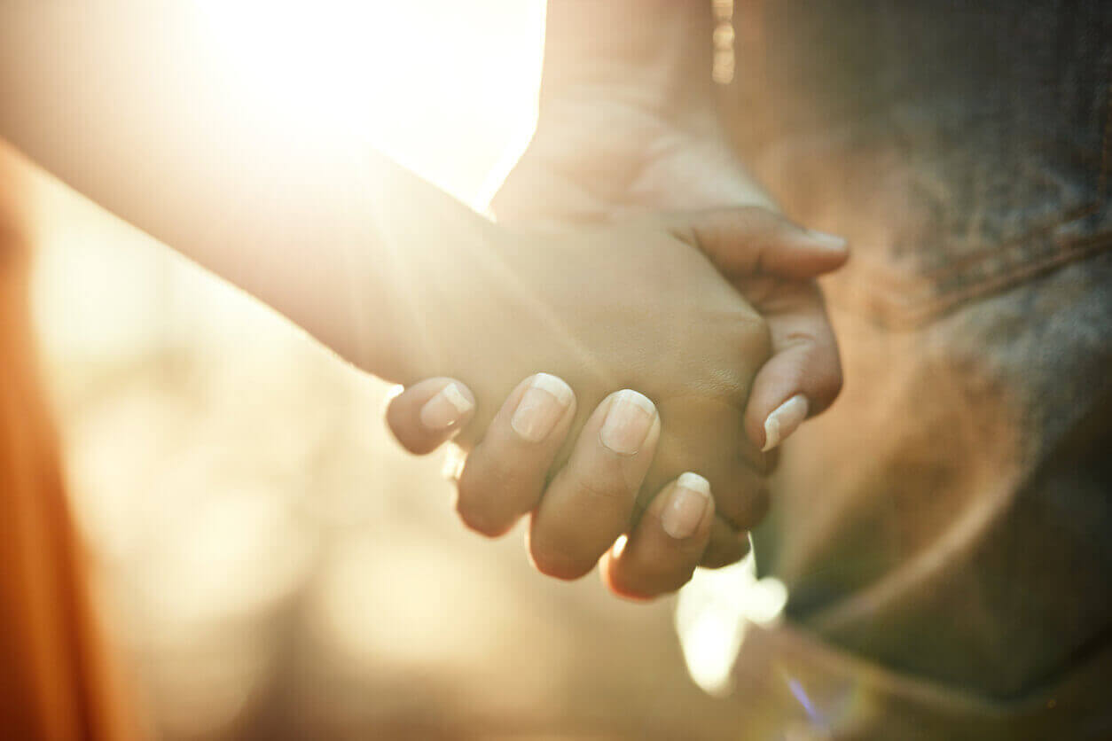 Domestic harassment support: two people holding hands in warm sunlight, with no faces shown