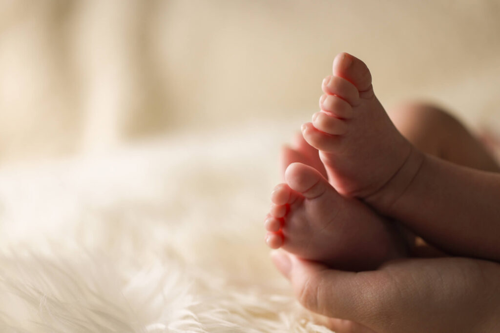 Adopt a child as a baby: a baby's bare feet held in an adult's hand