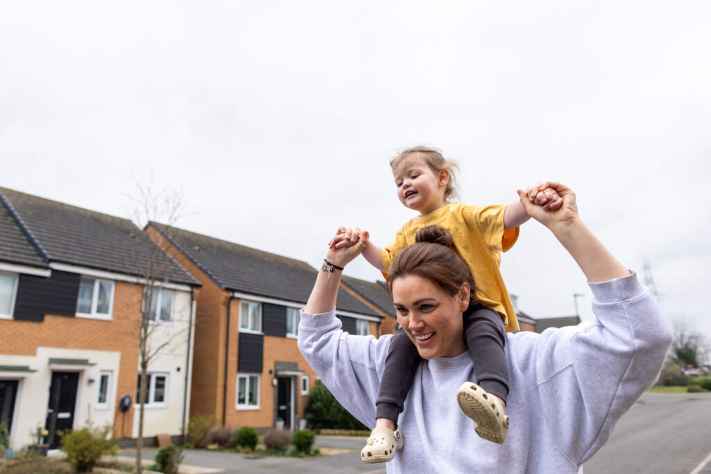 Form RX1 and the family home: a mother carrying her daughter on her shoulders outside a row of houses