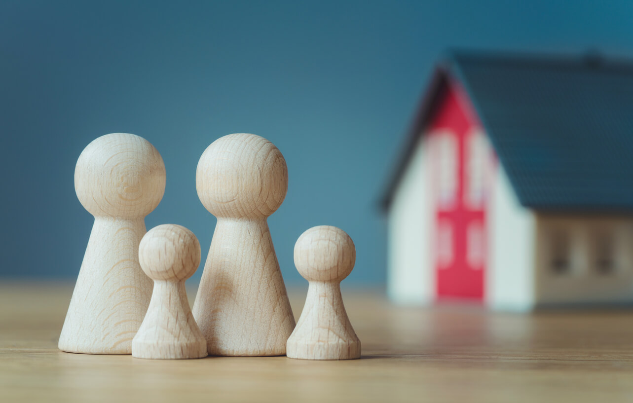Supervision order guide: four wooden family figures, two tall and two small, standing on a table in front of a model house